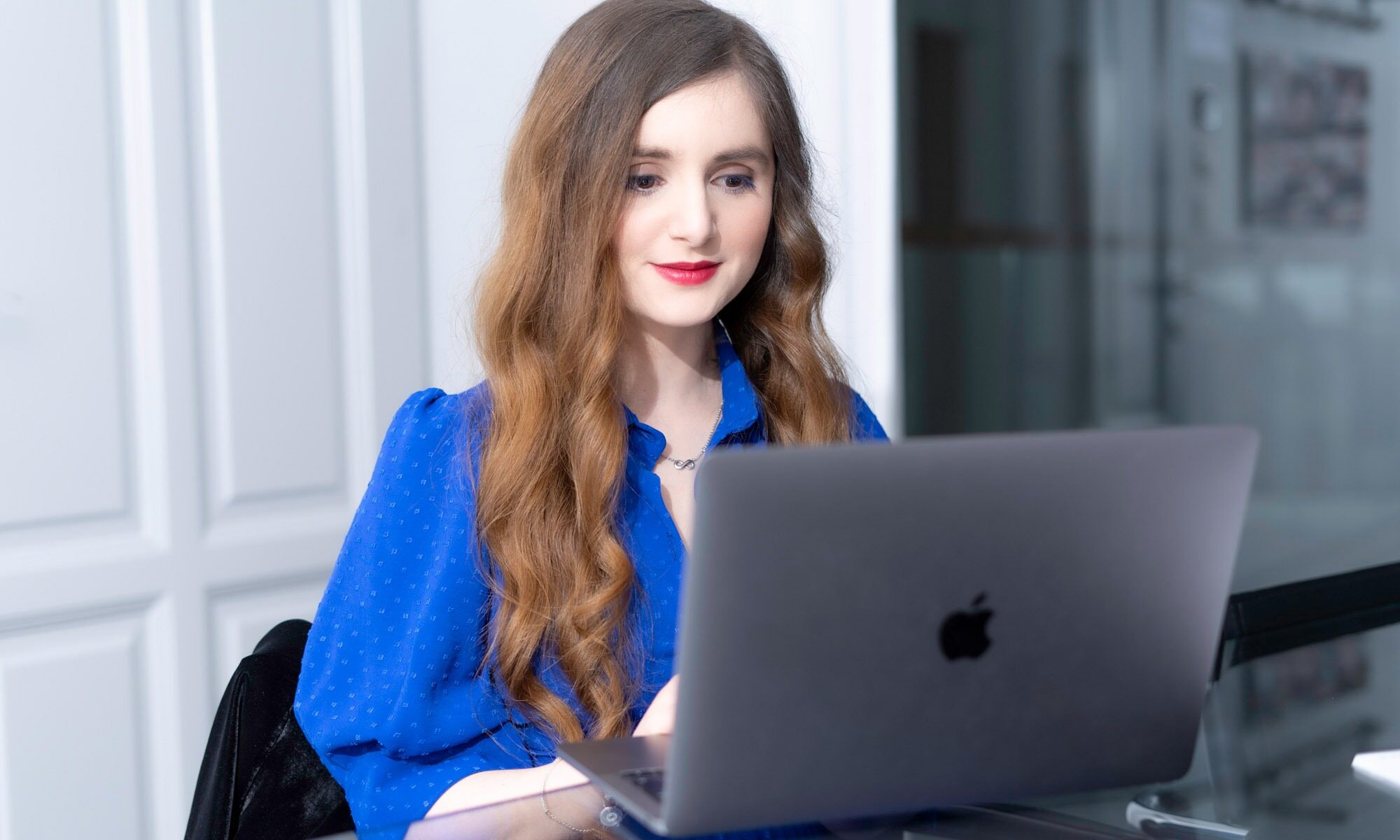 Lächelnde Frau im blauen Kleid sitzt am Apple Laptop