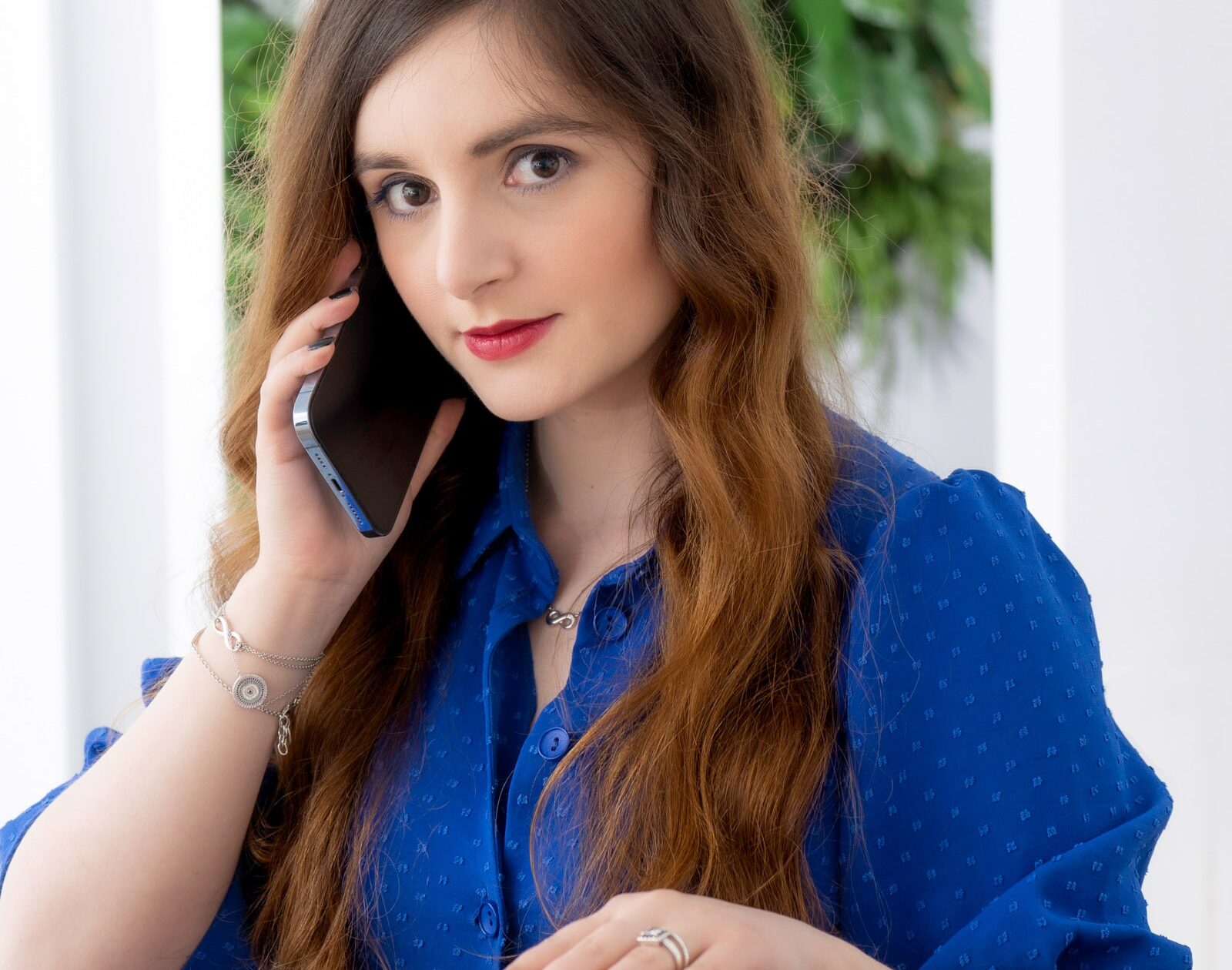 Lächelnde Frau im blauen Kleid sitzt am Tisch und spricht am Telefon